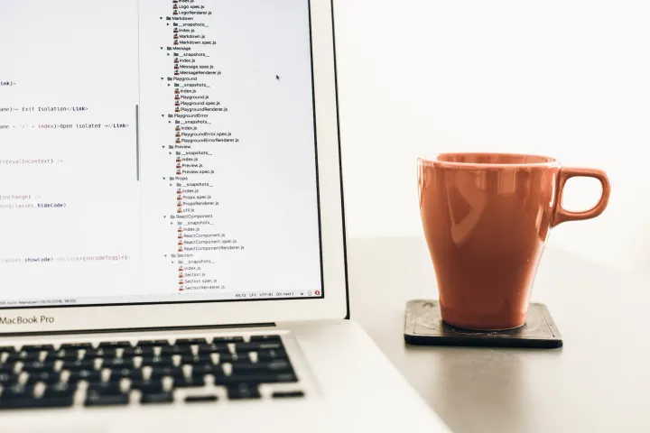 A MacBook laptop with a code editor open, next to a coffee mug